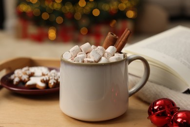Photo of Christmas cocoa with marshmallows and cinnamon sticks in grey cup on wooden tray indoors, closeup