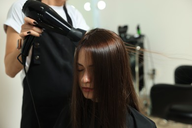 Photo of Hairdresser drying woman's hair in beauty salon