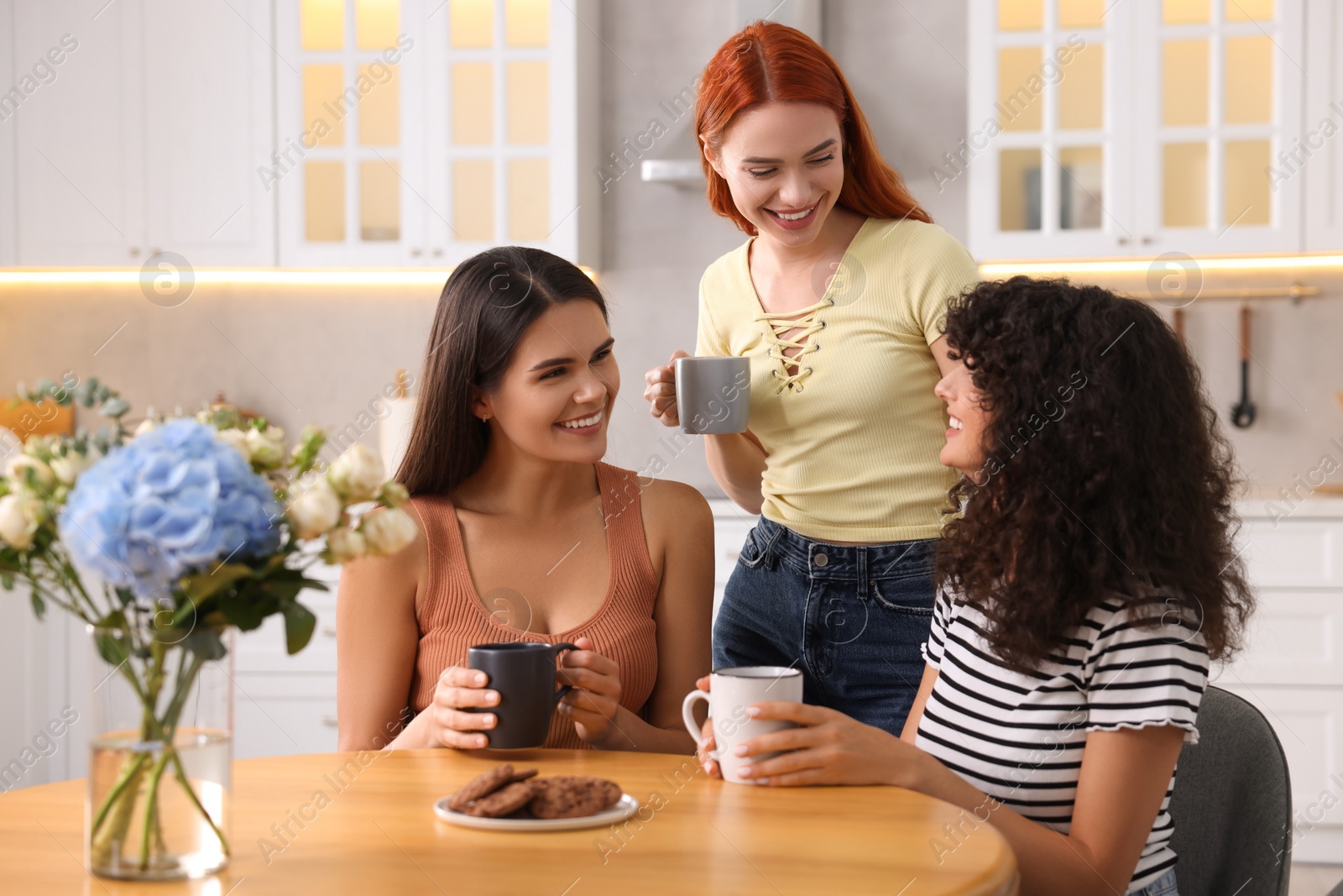 Photo of Happy young friends with cups of drink spending time together in kitchen