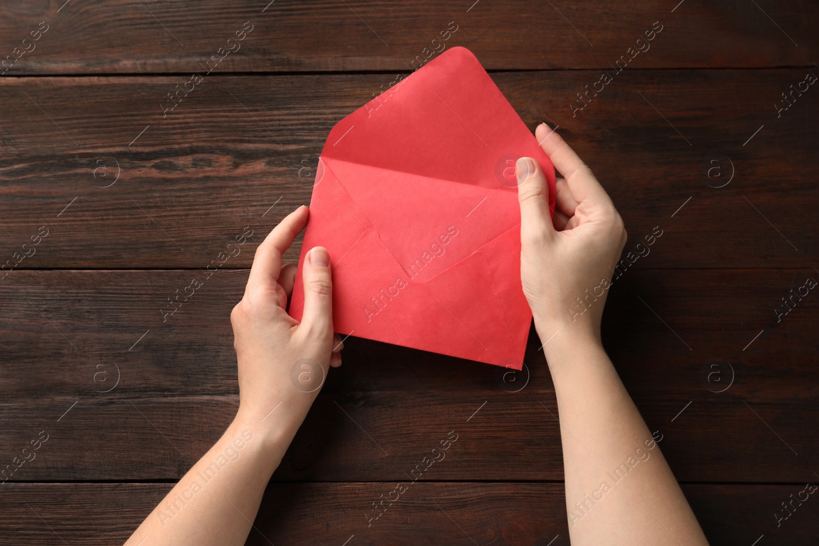 Photo of Woman with red paper envelope at wooden table, top view