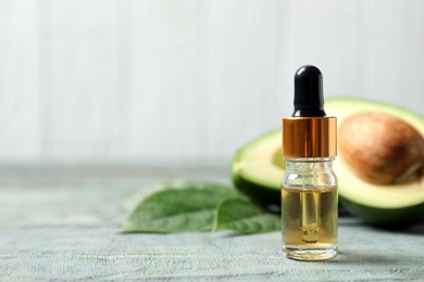 Bottle of essential oil and avocado on light blue wooden table. Space for text