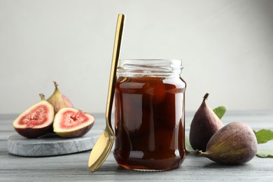 Photo of Jar of tasty sweet jam and fresh figs on grey table