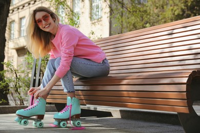 Photo of Woman lacing roller skates while sitting on bench outdoors