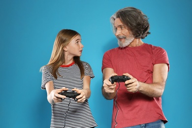 Photo of Mature man and teenage girl playing video games with controllers on color background