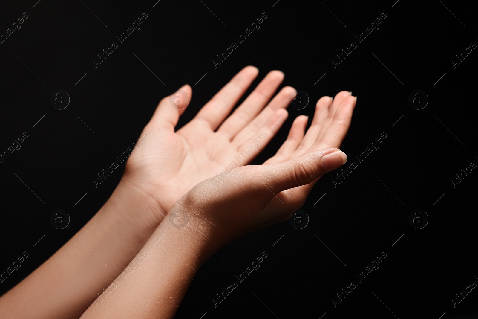 Photo of Woman stretching hands against black background, closeup