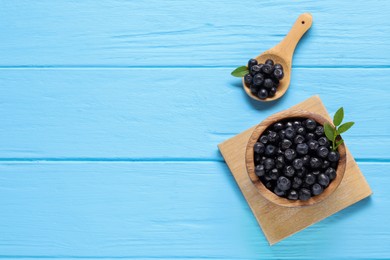 Photo of Ripe bilberries and leaves on light blue wooden table, flat lay. Space for text