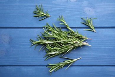 Photo of Sprigs of fresh rosemary on blue wooden table, flat lay