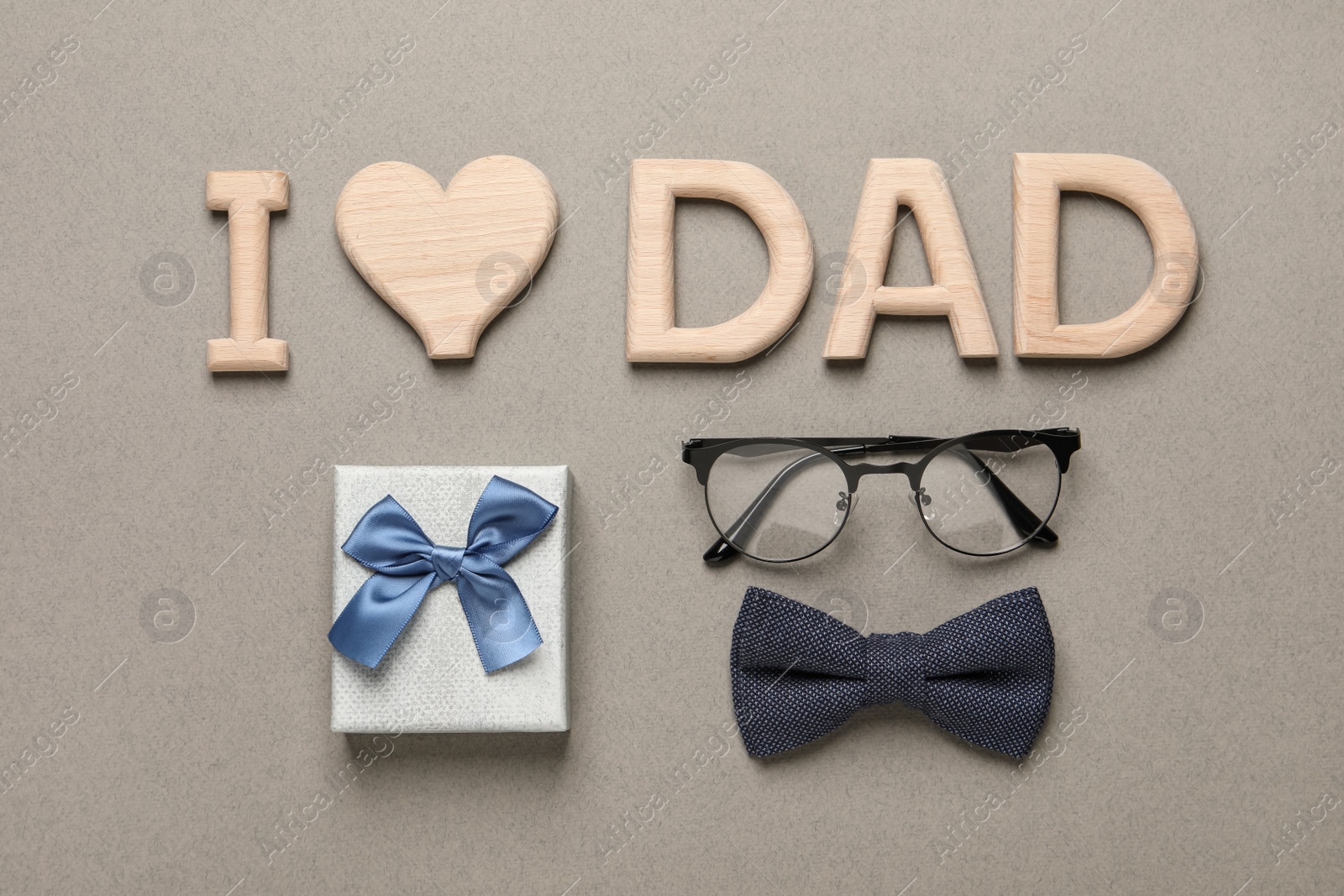 Photo of Phrase I love dad, gift box, eyeglasses and bow tie on grey background, flat lay. Father's day celebration