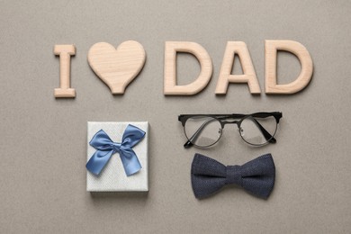 Photo of Phrase I love dad, gift box, eyeglasses and bow tie on grey background, flat lay. Father's day celebration