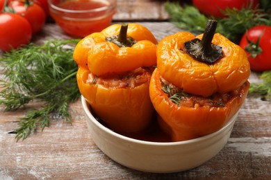 Photo of Tasty stuffed peppers in bowl on wooden table, closeup