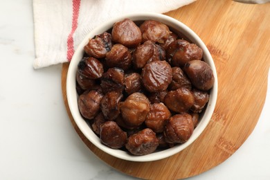 Roasted edible sweet chestnuts in bowl on white marble table, top view