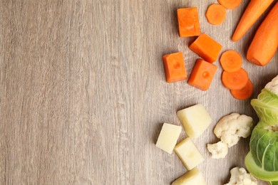 Photo of Carrot and cauliflower frozen purees cubes and fresh vegetables on wooden table, flat lay. Space for text