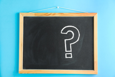 Blackboard with question mark hanging on light blue wall