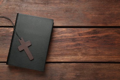 Photo of Wooden Christian cross and Bible on table, top view. Space for text