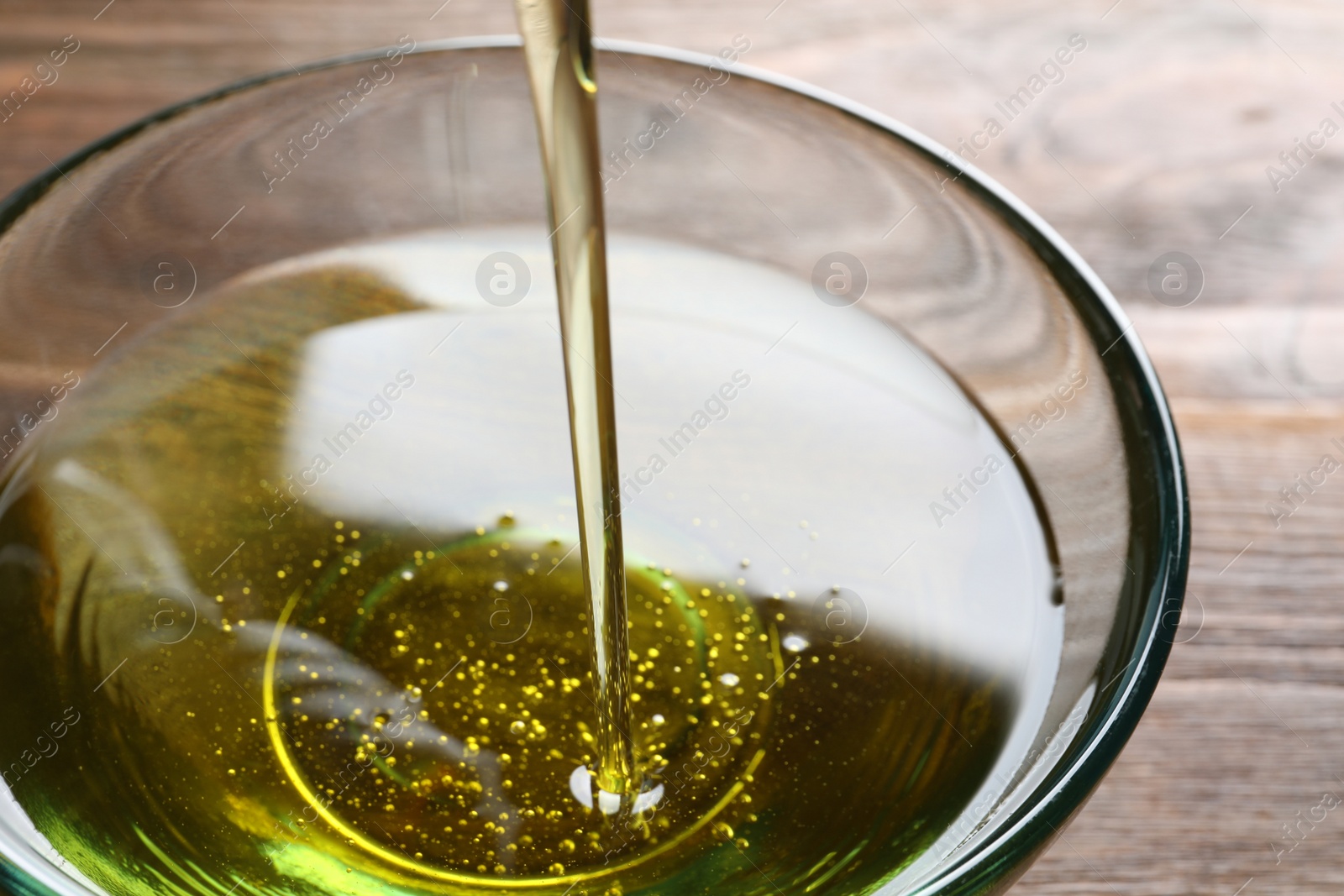 Photo of Pouring fresh olive oil into bowl on wooden background, closeup