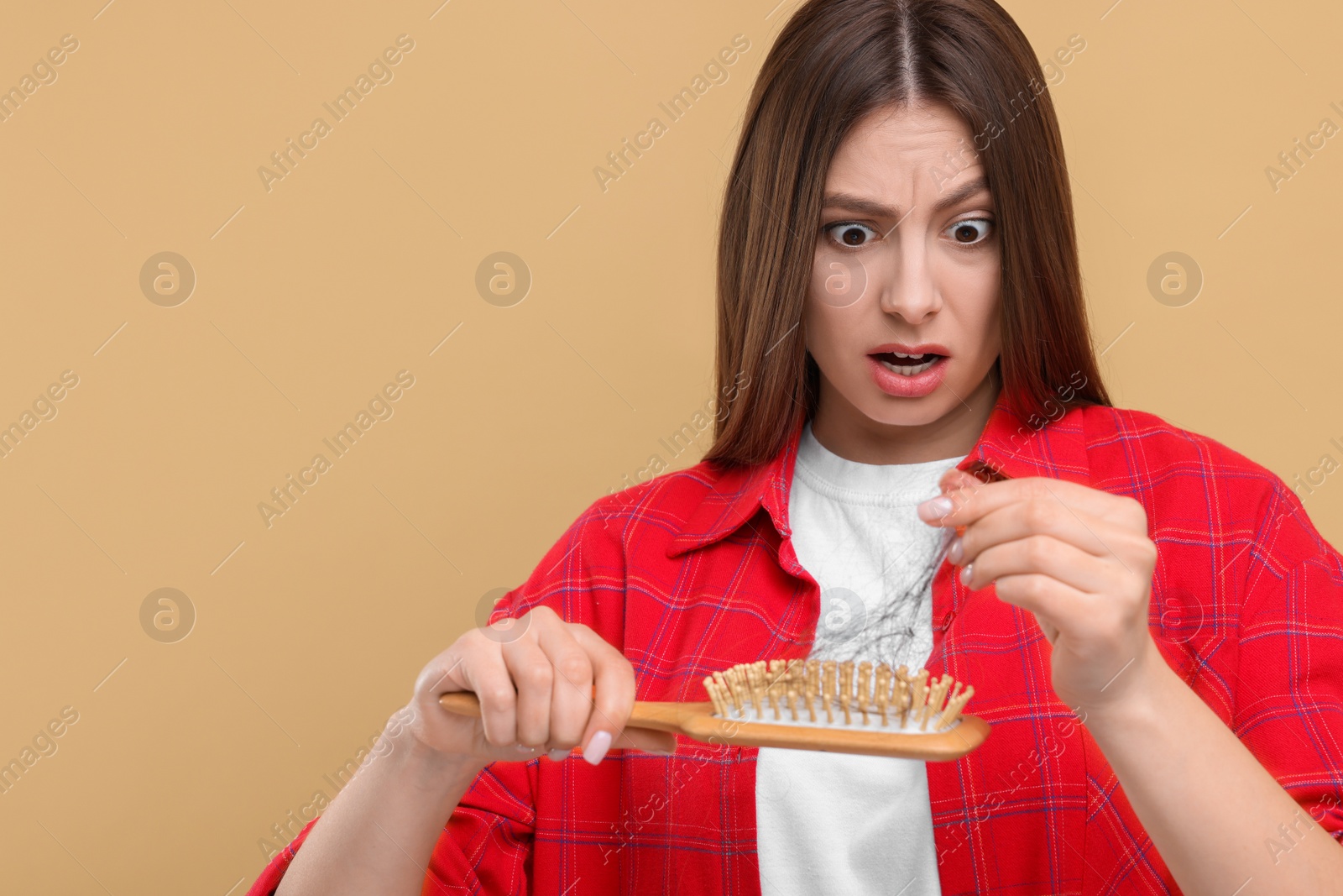 Photo of Emotional woman untangling her lost hair from brush on beige background, space for text. Alopecia problem