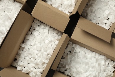 Photo of Open cardboard boxes with pieces of polystyrene foam on floor, flat lay. Packaging goods