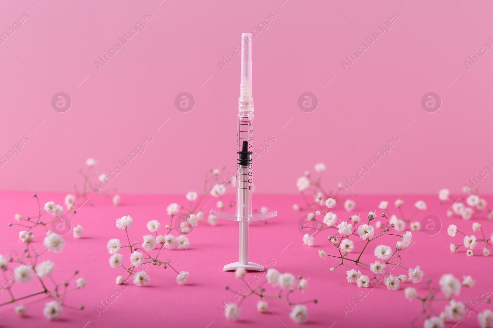 Photo of Cosmetology. Medical syringe and gypsophila flowers on pink background