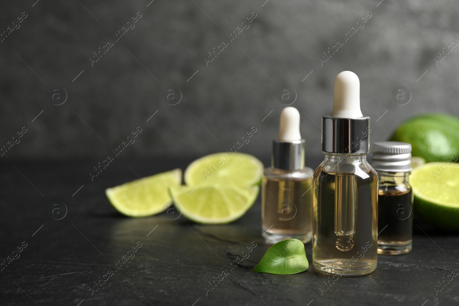 Photo of Lime essential oil and cut citrus fruits on black table. Space for text