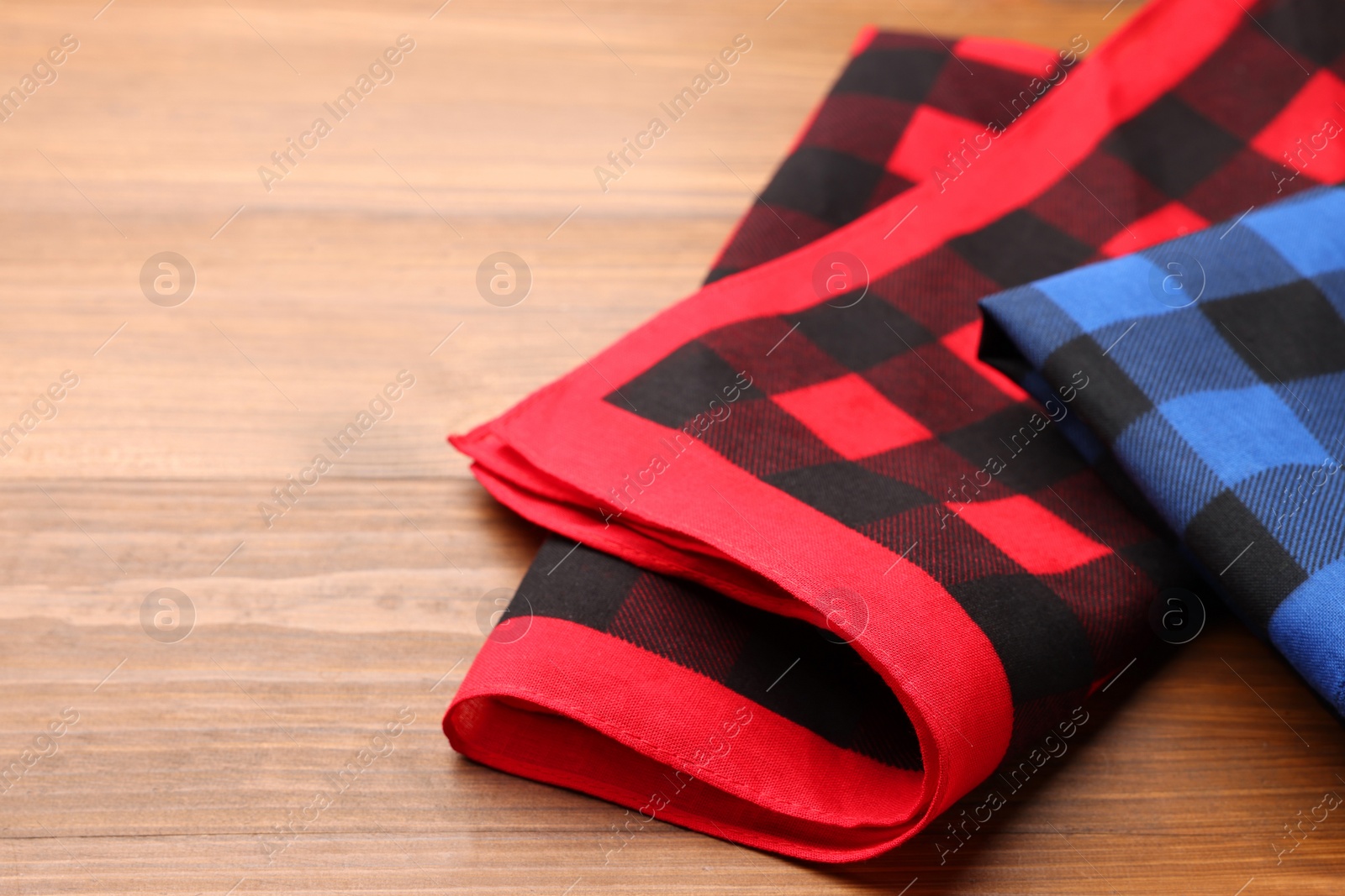 Photo of Folded red and blue checkered bandanas on wooden table, space for text