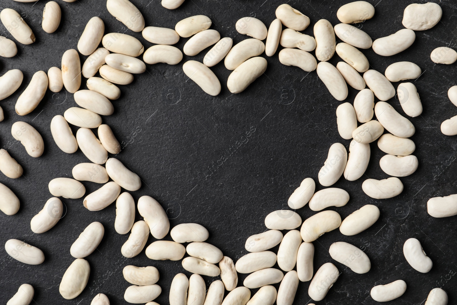 Photo of Heart shaped frame made of raw beans on black background, flat lay with space for text. Vegetable seeds