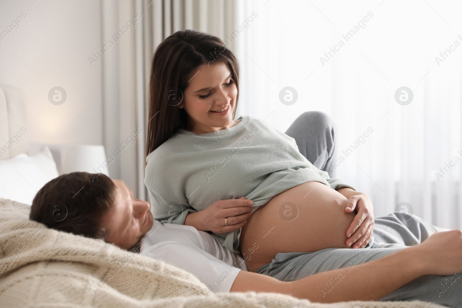 Photo of Young pregnant woman with her husband in bedroom