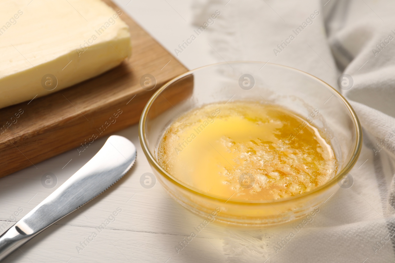 Photo of Melted butter in glass bowl and knife on white wooden table, closeup