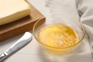 Photo of Melted butter in glass bowl and knife on white wooden table, closeup