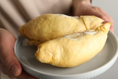 Photo of Woman holding plate with pieces of durian on light background, closeup