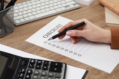 Photo of Woman filling Checklist at wooden table, closeup