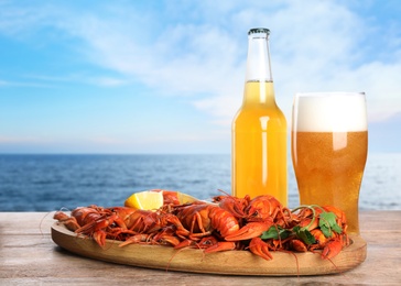 Image of Cooked crayfishes served with beer on wooden table near sea