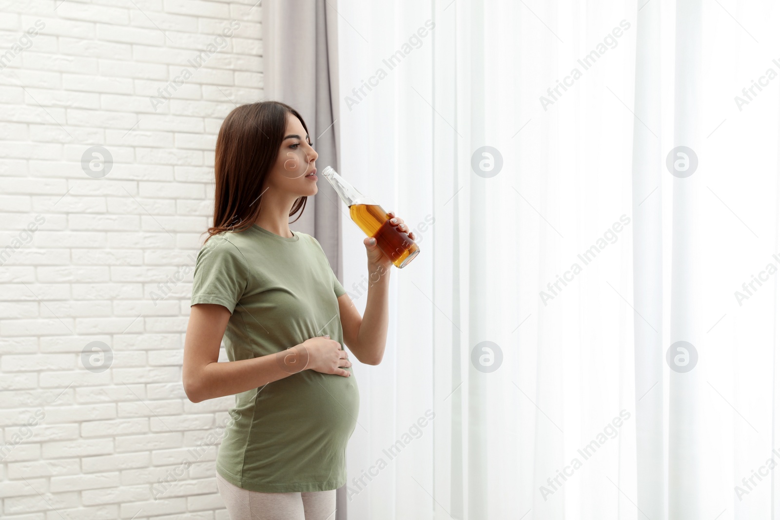 Photo of Pregnant woman with bottle of beer indoors, space for text. Alcohol abuse during pregnancy