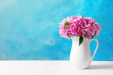 Photo of Pitcher with beautiful peony flowers on table against color background