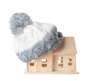 Photo of House model with knitted hat on roof against white background. Heating concept