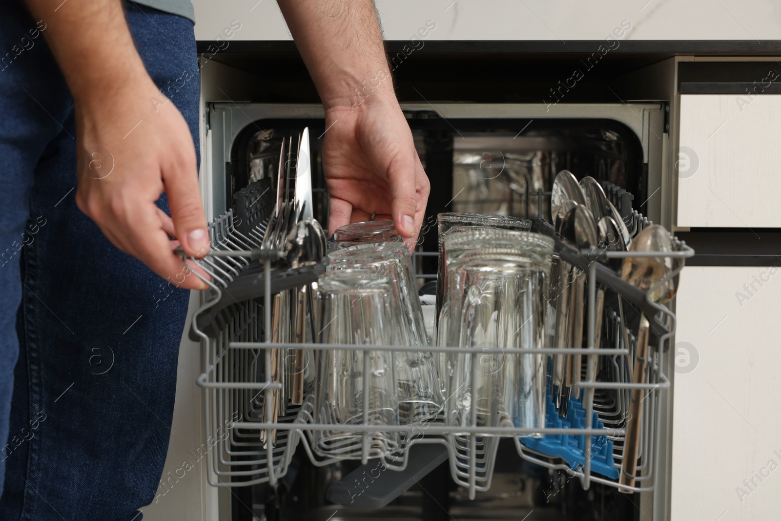 Photo of Man loading dishwasher with glass and cutlery indoors, closeup
