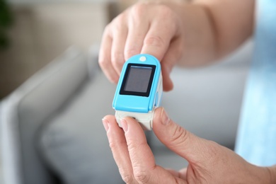 Photo of Mature woman checking pulse with medical device at home, closeup