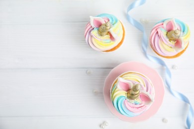 Photo of Cute sweet unicorn cupcakes on white wooden table, flat lay. Space for text