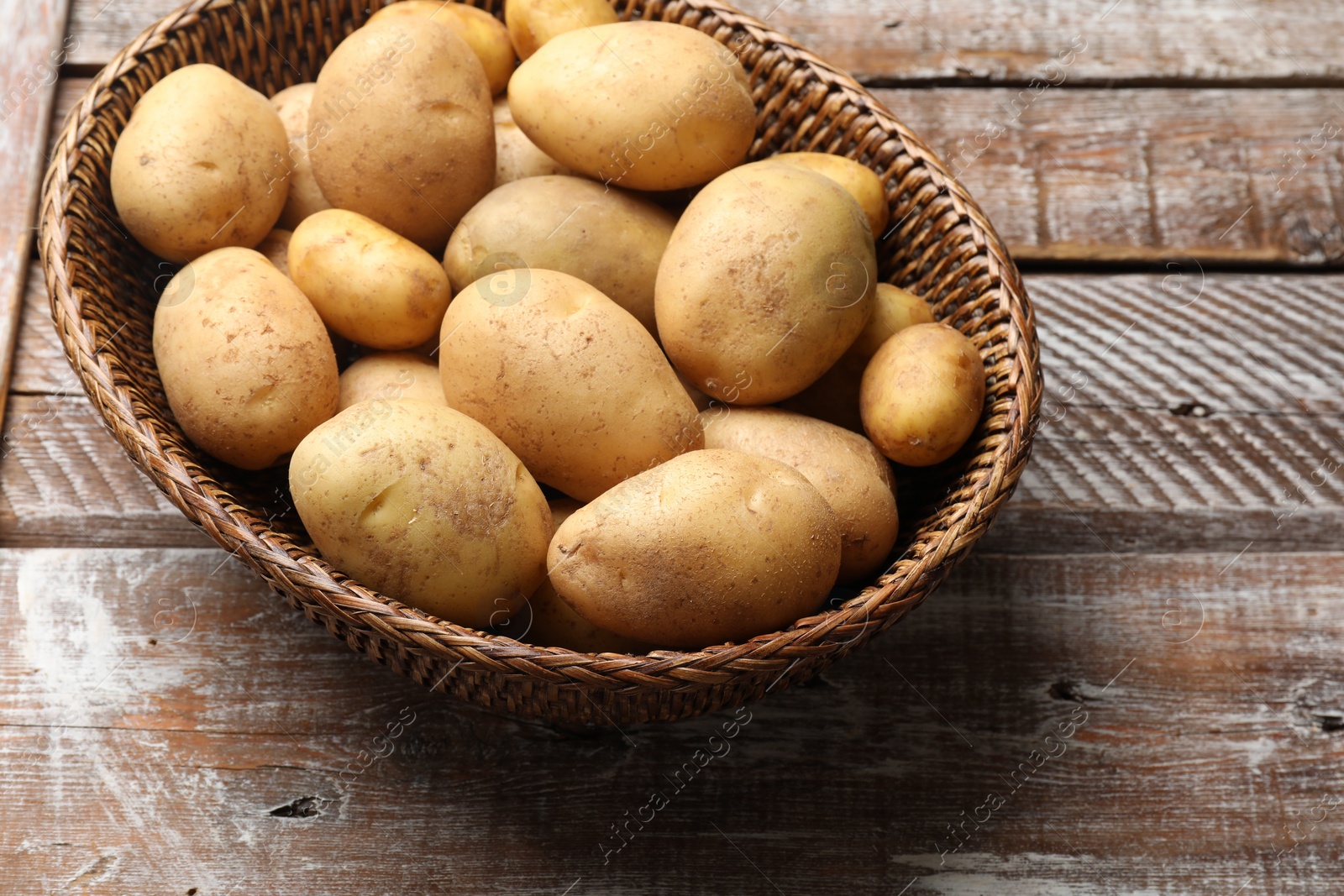 Photo of Raw fresh potatoes in wicker basket on wooden table