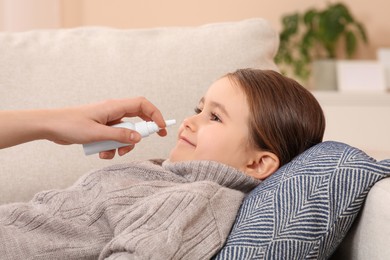 Mother using nasal spray to treat her little daughter on sofa, closeup