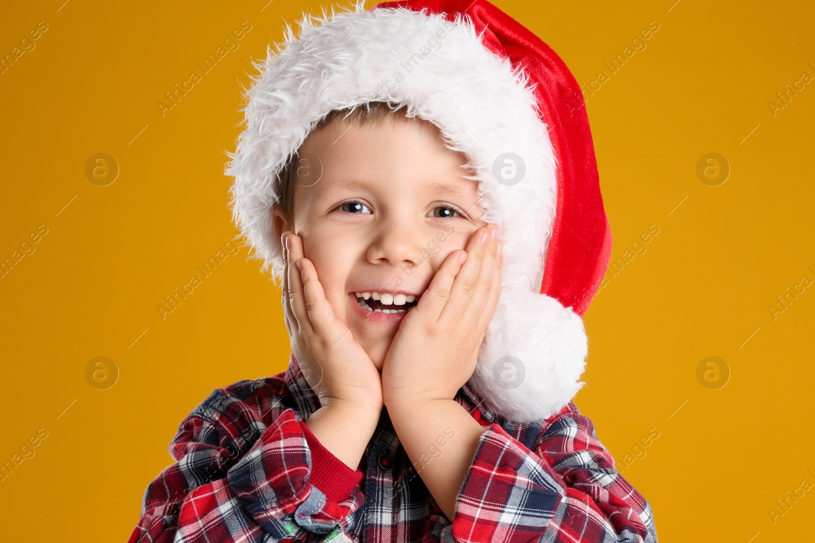 Photo of Cute child in Santa hat on yellow background. Christmas celebration