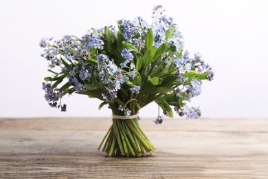 Photo of Bouquet of beautiful forget-me-not flowers on wooden table against white background