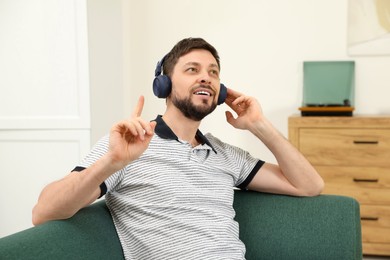 Handsome man in headphones enjoying music on sofa indoors