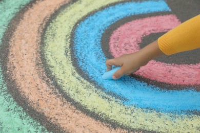 Child drawing rainbow with chalk on asphalt, closeup