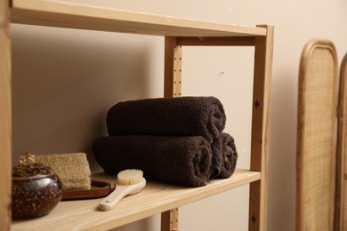 Soft towels, brush and loofah on wooden shelf indoors, closeup