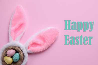 Image of Easter bunny ears headband and dyed eggs in nest on pink background, flat lay