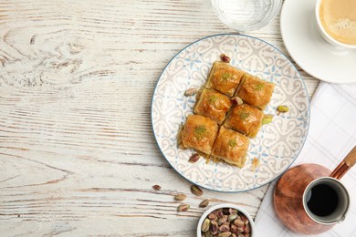 Delicious baklava with pistachios, nuts and hot coffee on white wooden table, flat lay. Space for text