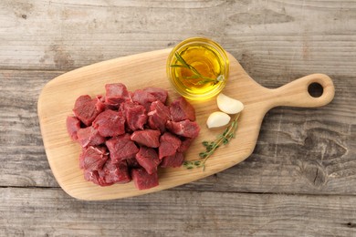 Pieces of raw beef meat, oil and garlic on wooden table, top view