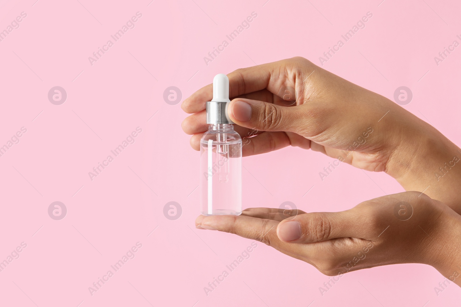 Photo of Woman with bottle of cosmetic serum on pink background, closeup. Space for text