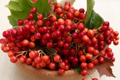 Photo of Bowl with tasty viburnum berries on white wooden table, closeup