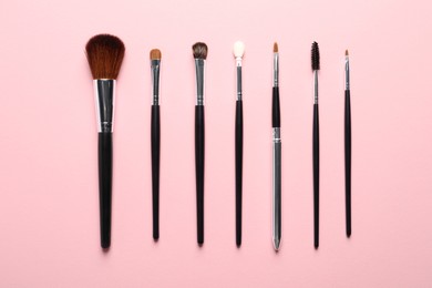 Photo of Different makeup brushes on pink background, flat lay